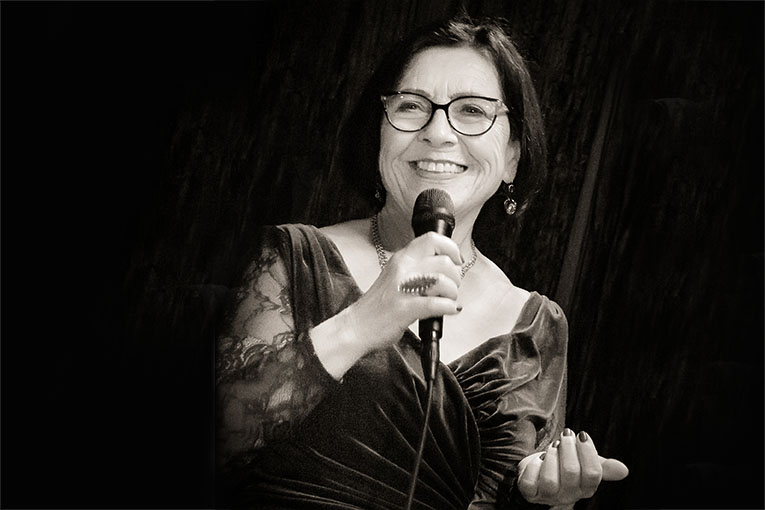 Die Sängerin Marina Thalke vor dunklem Hintergrund mit Mikrofon in der Hand und lächelnd.