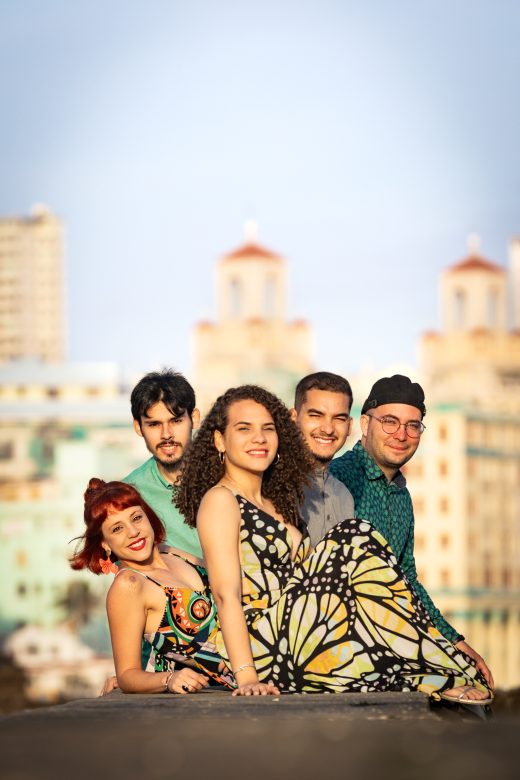 Die fünf Musiker von Espirales lächeln in die Kamera, sie stehen vor einer Stadtkulisse unter einem blauen Himme.