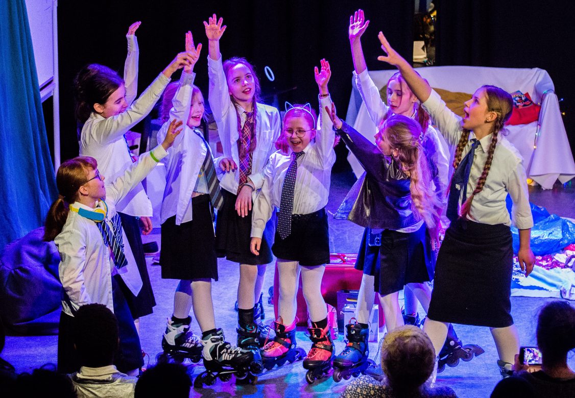 Gruppe Kinder auf der Bühne. Sie tragen einen schwarzen Rpck und ein weiés Hemd mit Krawatte