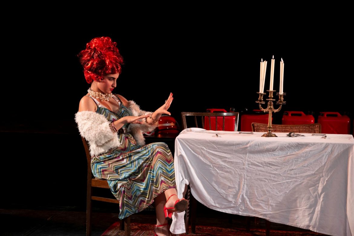 Ein Kind als Frau verkleidet, mit roter Perücke an einem gedeckten Tisch mit einem Kerzenleuchter