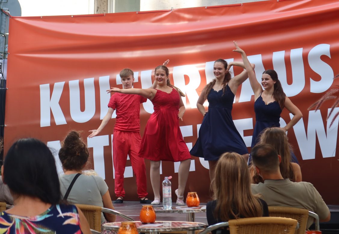 Drei Tänzerinnen und ein Tänzer präsentieren sich auf einer Open-Air-Bühne in verschiedenen Posen.