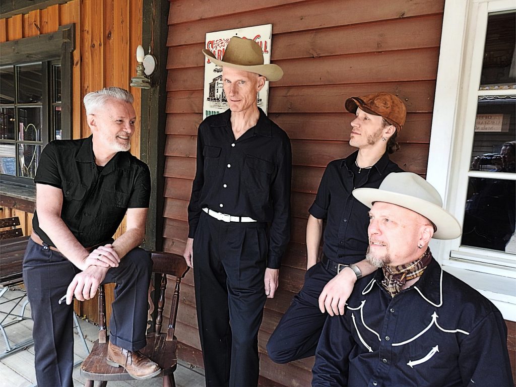 Bandfoto der Band The mountain shouts: vier Musiker vor einer Berghütte