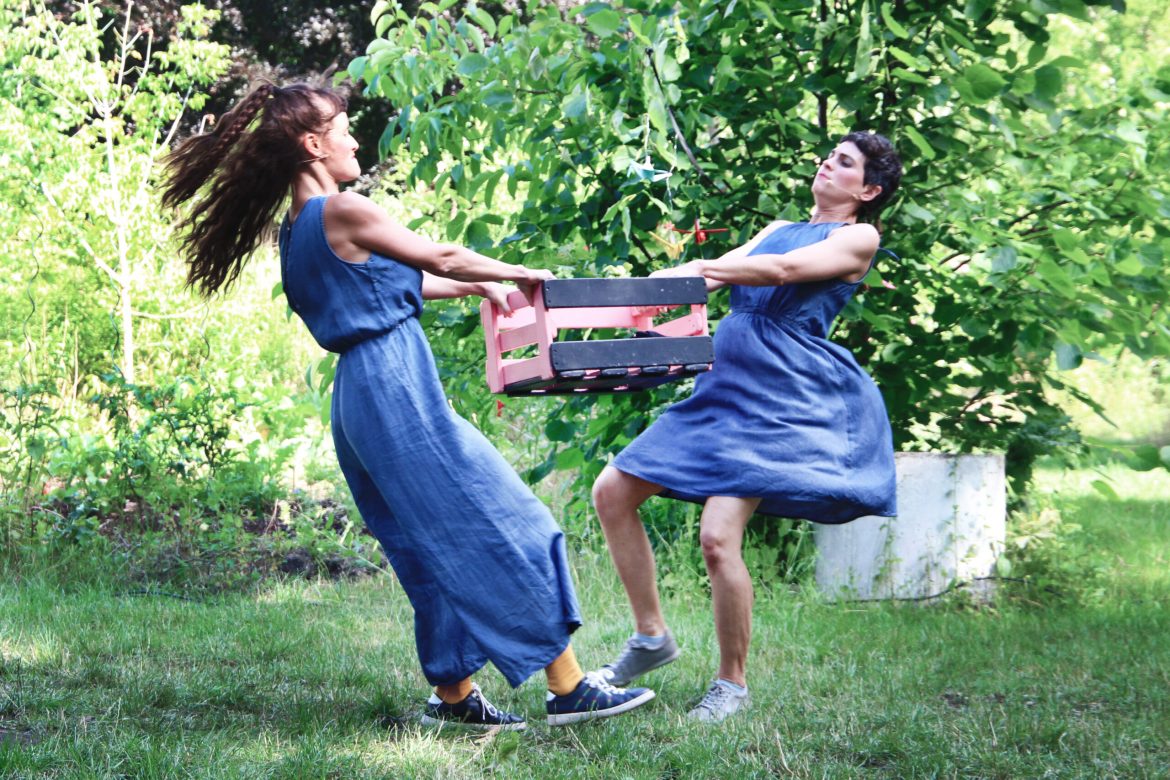 Zwei Schauspielerinnen in einem Garten streiten sich um eine Kiste