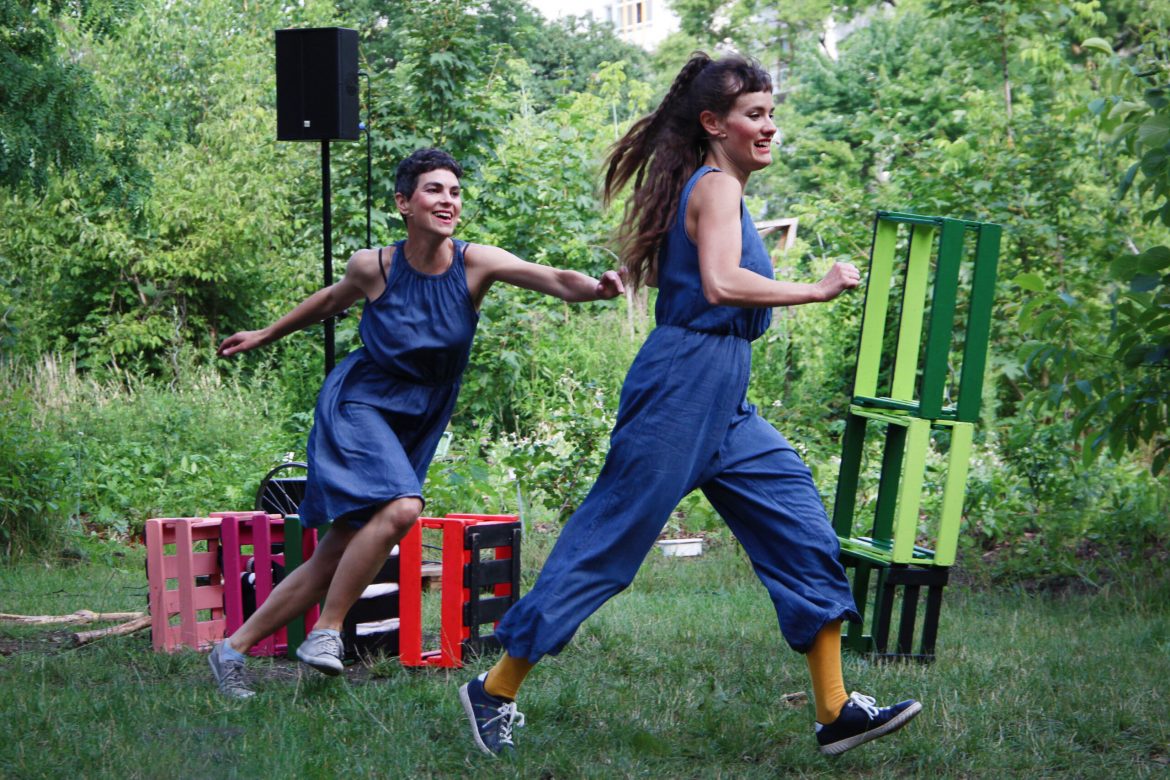 zwei lachende Schauspielerinnen laufen durch einen Garten