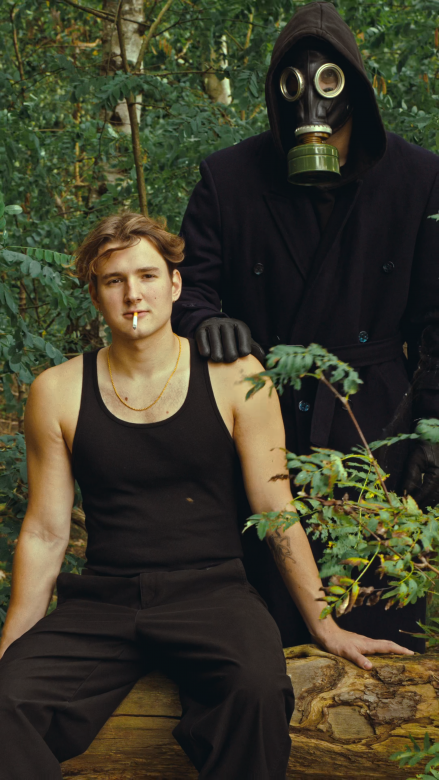 Ein Mann im Vordergrund, im Hintergrund steht jemand mit Gasmaskella